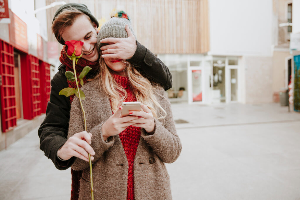 un homme cache les yeux d'une femme et lui tend une rose