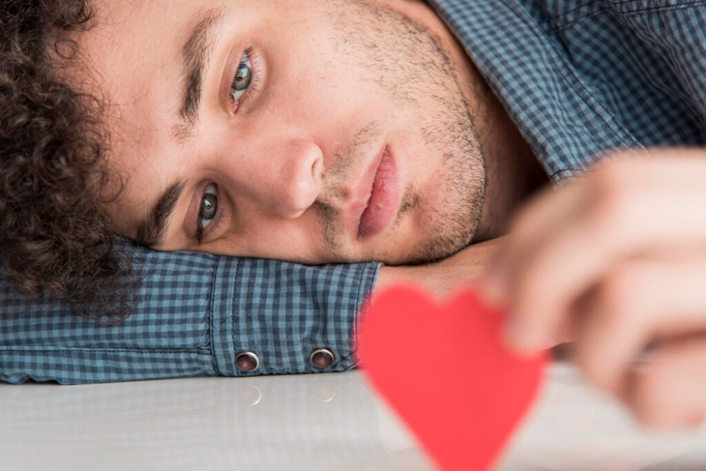 un homme triste allongé avec un coeur en papier dans les mains