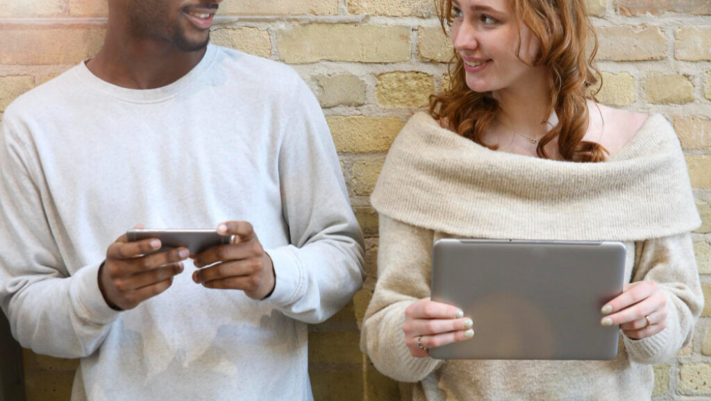 un garçon avec son téléphone à coté d'une fille avec un ordinateur