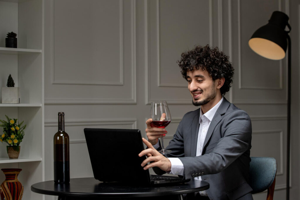 homme en costume avec un verre de vin devant son ordinateur