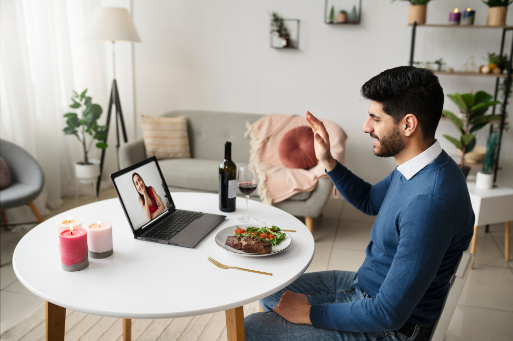 un homme mange et salue une femme en visio sur son ordinateur